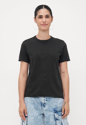 Zwarte katoenen T-shirt met korte mouwen, voorzien van geborduurde hartpatronen. Ronde hals, relaxte pasvorm, gecombineerd met blauwe denim cargobroek.