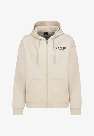 Beige zip-up hoodie with a drawstring hood, front pockets, and "EXPECT NOTHING" printed in black on the left chest area.