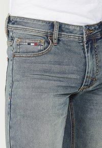 Világoskék, slim fit farmernadrág, sárga varrással, egy kis, színes folttal a zsebében, és klasszikus ötpocketes dizájnnal.