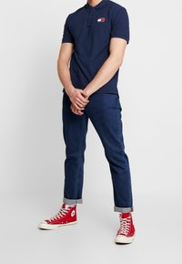 Námořnická polo košile s krátkým rukávem, vyznačující se malým logem v červené a bílé barvě. Nosit s tmavě modrými džínovými kalhotami a červenými teniskami na vysoké podrážce.