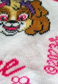 Tissu tricoté avec un fond blanc présentant le visage d'un chien de dessin animé en marron et noir, avec des accents et des lettres roses. Le texte a un design ludique.