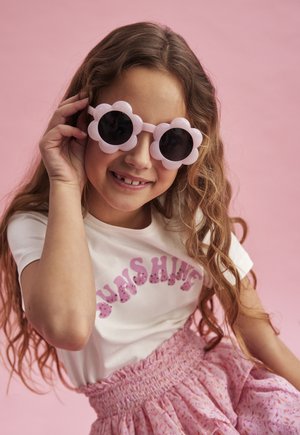Rosa blommformade solglasögon med svarta linser. Vit t-shirt med "SUNSHINE" i rosa paljetter. Rosa mönstrad kjol med smockad midja.
