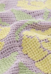 Gros plan d'un tissu crochet texturé avec des motifs floraux jaunes et des feuilles vertes sur fond lavande.