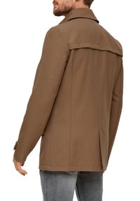 Braune Stoffjacke mit strukturiertem Kragen, Rückenpasse und seitlichen Schlitzen. Verfügt über eine glatte Struktur und eine taillierte Passform. Kombiniert mit grauen Jeans.