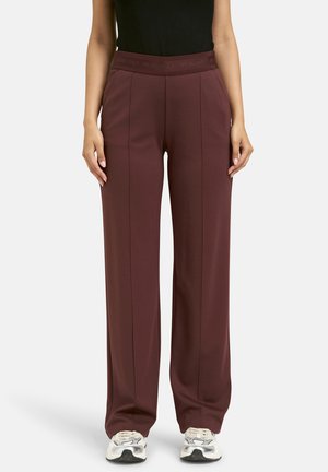 Burgundy wide-leg trousers made of soft fabric, featuring a high waistband with embossed lettering and front pleats. Styled with sneakers.