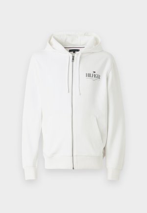 Hvit jakke med glidelås, kenguru-lomme, justerbar hette med snøring og brodert "HILFIGER"-logo i svart. Laget av bomull, med ribbestrikkede mansjetter.