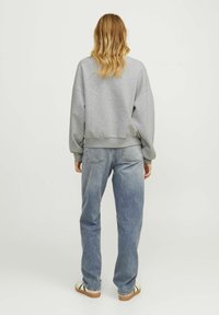 Sweatshirt grigio a maniche lunghe con spalle basse, abbinato a jeans azzurri a vita alta e sandali beige con accenti scuri.