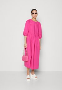 Rosa kjole med puffede ærmer og snøret talje, hvide block-heeled sandaler og en lille rosa håndtaske. Glat stof med en afslappet pasform.