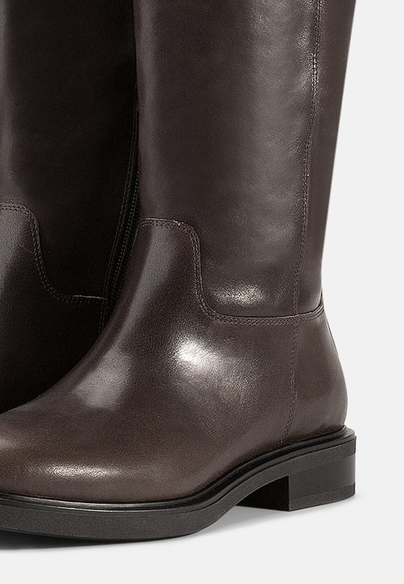 Bottes en cuir marron arrivant au genou présentant une finition lisse et un petit talon carré ; couture minimale et design simple sans accents de matériel.