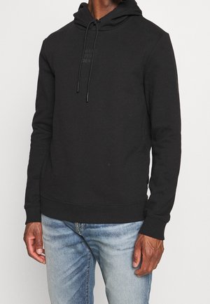 Svart hoodie av mjukt tyg, med dragsko i huvan, ribbade ärmslut och en subtil prägling av logotypen på bröstet.