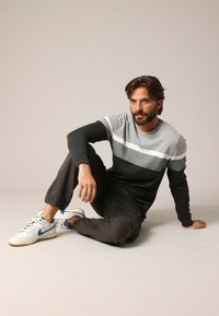 Donkergrijs en lichtgrijs gestreepte trui met een ronde hals, gecombineerd met donkere broeken en witte sneakers, tegen een neutrale achtergrond.