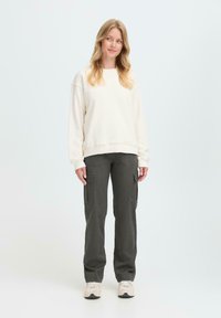 Krämfärgad sweatshirt, grå cargobyxor med sidofickor och beige sneakers. Mjuk, avslappnad tygkvalitet med en ledig passform och rak bendesign.
