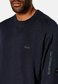 Felpa blu navy realizzata in cotone, con collo a girocollo, un discreto logo "BOSS" sul petto e una tasca con zip sul maniche sinistro.