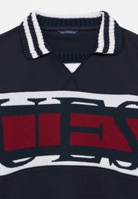 Μπλε ναυτική πόλο μπλούζα με λευκό και κόκκινο πλεκτό γιακά. Διαθέτει μεγάλο λογότυπο στο στήθος σε αντίθετα χρώματα. Μαλακή υφή, casual σχεδιασμός.