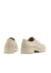 Beżowe skórzane buty o teksturowanym wykończeniu, niskim kroju, kontrastującymi sznurowadłami oraz grubymi, solidnymi podeszwami w stylu platformy.
