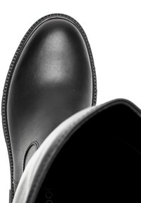 Czarny gumowy botek za kostkę o gładkiej powierzchni, okrągłym nosku i teksturowanej podeszwie. Posiada wnętrze wyłożone podszewką oraz detal w postaci bocznych wycięć.