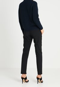Pull en maille bleu marine, coupe décontractée, texture côtelée ; pantalon noir ajusté avec une coupe slim ; sandales noires à talons hauts avec brides autour de la cheville.