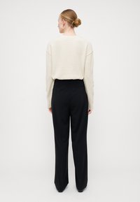 Abbigliamento da casa con un maglione crema oversize dal tocco morbido, abbinato a pantaloni neri a vita alta e gamba larga.