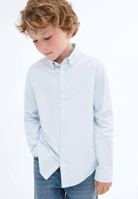 Cămașă cu dungi albastre deschise și albe, cu guler, mâneci lungi și butoane albe; purtată cu blugi.