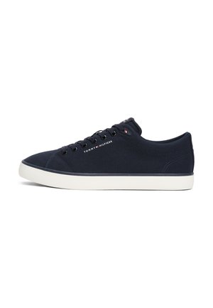 Donkerblauwe lage sneaker met witte zool, zwarte veters en "Tommy Hilfiger" tekst en logo aan de zijkant en op de tong.
