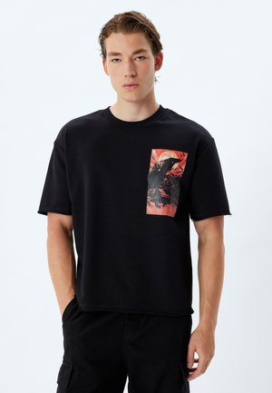 Black cotton t-shirt with a round neckline, featuring a large red and black graphic print on the left side and raw edge sleeves.
