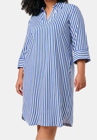 Robe rayée avec des rayures verticales bleues et blanches, col à revers, manches trois-quarts et fentes latérales à l'ourlet. Fabriquée en tissu léger.