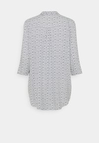 Bluzka z długim rękawem w czarno-białym abstrakcyjnym wzorze geometrycznym, luźny krój i lekko zaokrąglony dół.