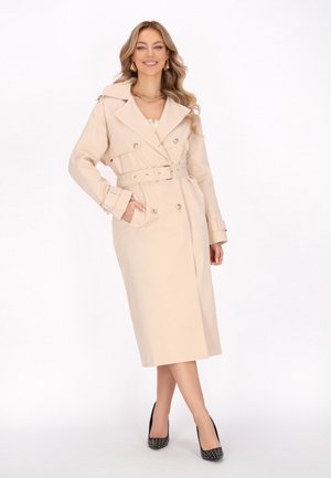 Beige trench coat with a double-breasted front, belted waist, and flap pockets. Features a wide collar and long sleeves. Black heels.