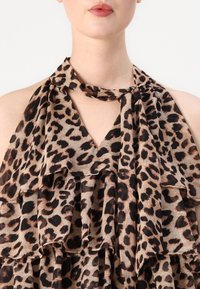 Løveprint halterneck top i let stof, med voluminøse lag og en bundet halsudskæring. Farvepaletten inkluderer beige, sort og brun.