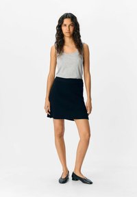 Graues ärmelloses Oberteil kombiniert mit einem dunkelblauen, gerippten Strickrock. Der Rock hat ein aufflatterndes Design und einen Bund, dazu werden schwarze Ballerinas getragen.