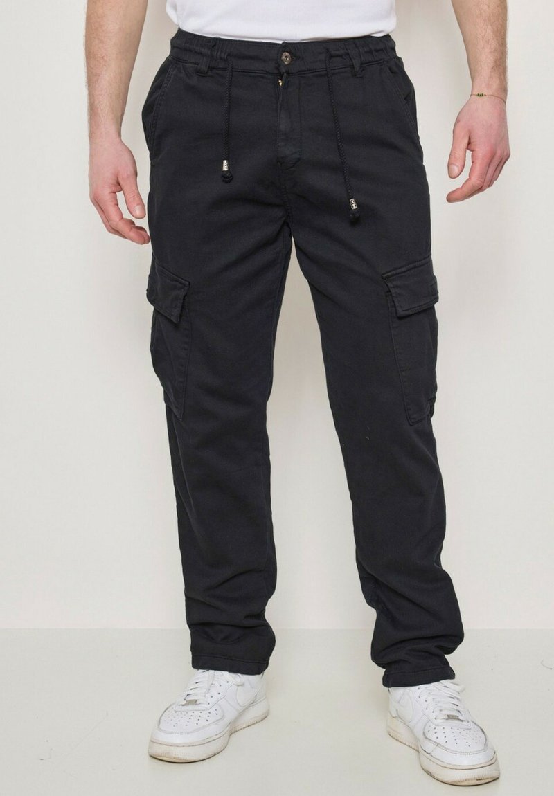 Pantalons cargo noirs en coton, dotés d'une taille avec cordon de serrage ajustable, de poches latérales et d'une coupe décontractée. Portés avec des baskets blanches.