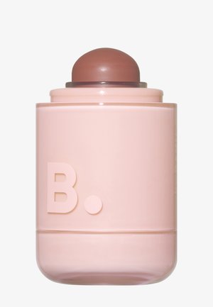 Pink zylindrischer Kosmetikbehälter mit einem abgerundeten bräunlichen Applikator oben und mit dem geprägten Buchstaben „B.“ vorne.