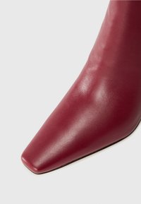 Stivale bordeaux con tacco alto e punta affusolata, realizzato in pelle liscia, caratterizzato da un design elegante e minimalista.