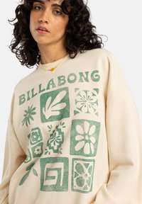 Billabong crèmekleurige sweatshirt met groene grafische prints, waaronder bloemen en vormen, met een relaxte pasvorm en geribbelde nek.