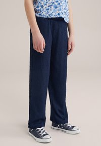 Navy blue, crinkled fabric pants with a loose fit, elastic waistband, and side pockets, paired with navy sneakers.
