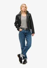 Czarna skórzana kurtka motocyklowa, szary t-shirt, niebieskie dżinsy o wysokim stanie i czarne buty sznurowane. Swobodny strój z podwiniętymi mankietami.