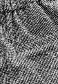 Texturovaná látka v šedé a bílé barvě s tkaným vzorem a mírným elastickým efektem. Obsahuje jemný, měkký povrch a detail se shromážděným pasem.