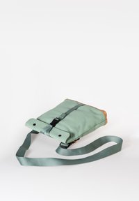 Borsa verde menta con dettagli in pelle marrone, forma rettangolare, tracolla regolabile e chiusura a fibbia. Texture liscia e design minimal.