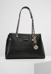 Sac à main en simili cuir noir avec un extérieur à motifs, des anses en chaîne argentée et des charms décoratifs. Il présente une plaque logo à l'avant.