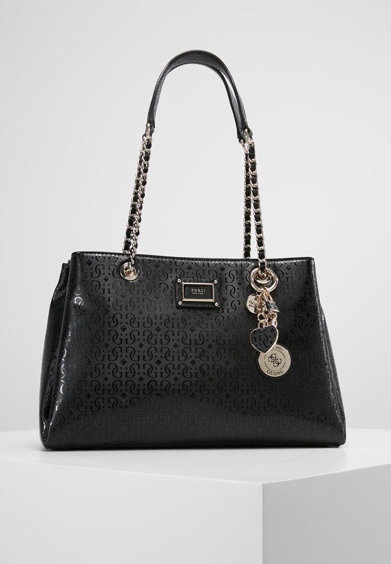 Sac à main en simili cuir noir avec un extérieur à motifs, des anses en chaîne argentée et des charms décoratifs. Il présente une plaque logo à l'avant.