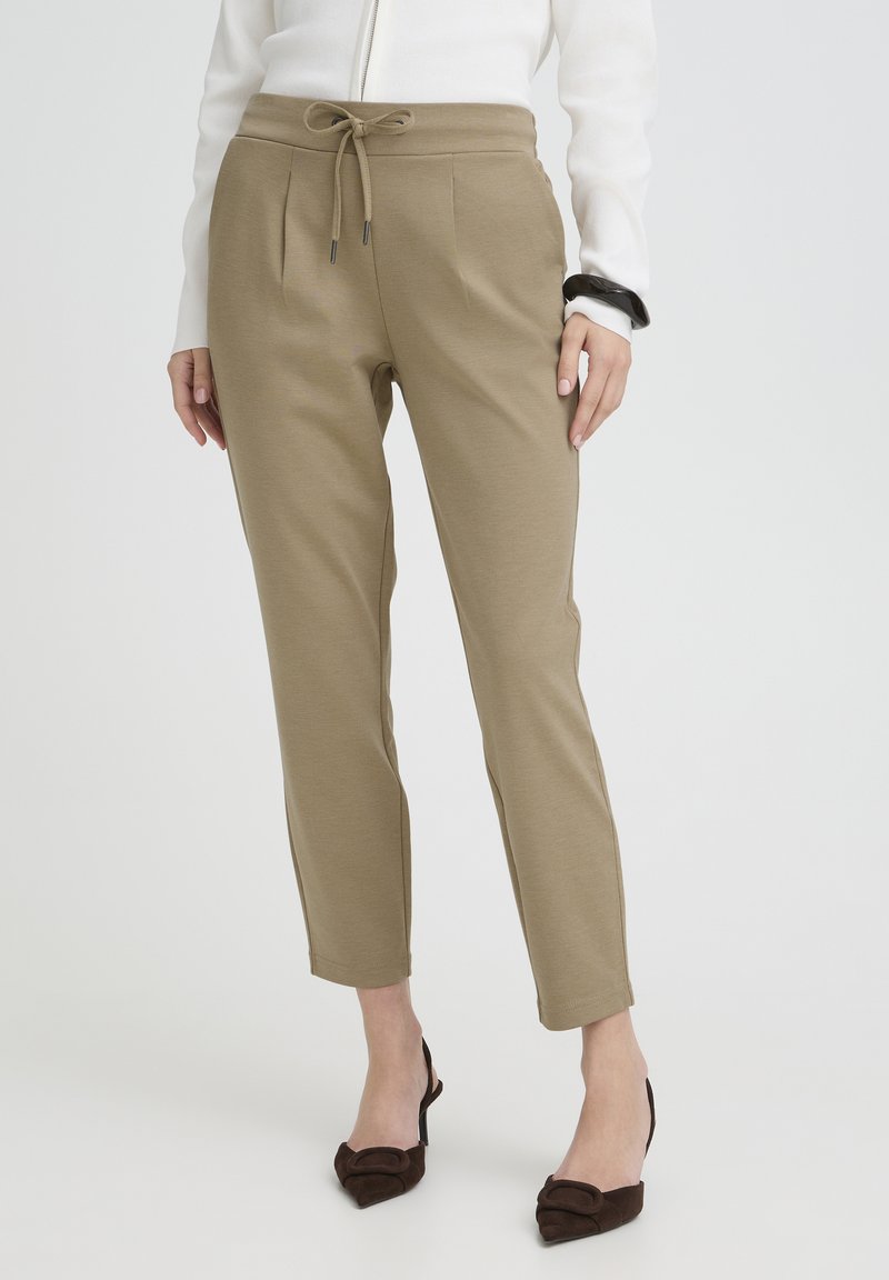 Beige elastic waist pants with a drawstring, featuring side pockets and tapered legs, paired with brown heeled shoes.