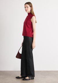 Top rosso senza maniche abbinato a jeans neri a vita alta e a gamba larga, con una piccola borsa bordeaux e scarpe nere con fibbia.
