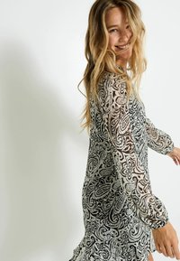 Vestido negro y blanco con estampado de paisley, mangas largas transparentes y una silueta fluida. La tela ligera y texturizada añade interés visual.