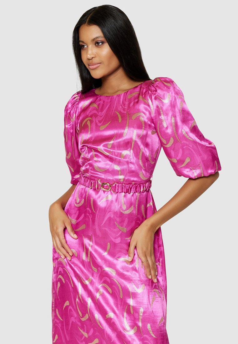 Abito di raso fucsia con maniche a sbuffo, vita arricciata e motivi a spirale dorati. Texture liscia e design lungo fino alla caviglia.