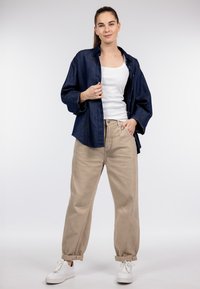 Marineblauw spijkershirt, wit tanktopje, beige broek met hoge taille en witte sneakers. Losse pasvorm met opgerolde manchetten en knoopdetails op het shirt.