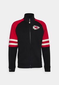 Schwarze Zip-Jacke mit roten Ärmeln, weißen Doppelstreifen an den Armen und Kansas City Chiefs-Logo auf der Brust.