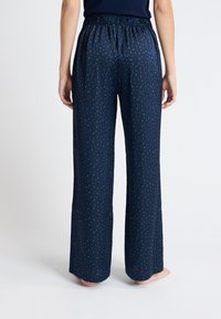 Marineblauwe pyjamabroek van een zachte, vloeiende stof; heeft een groen abstract patroon en een elastische tailleband. Wijde pijpen voor extra comfort.