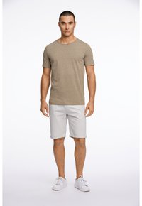 Avslappnad brun skjorta med korta ärmar, gråa shorts och vita sneakers. Skjortan har rund halsringning, och shortsen är uppvikta vid fållen.