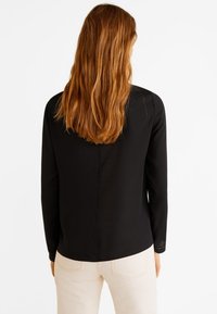 Schwarzes Langarmshirt mit rundem Halsausschnitt, glatter Textur und subtilen Nahtdetails. Die Rückansicht zeigt einen geraden Schnitt und keinerlei sichtbare Metallteile.