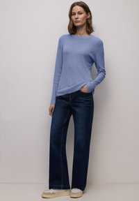 Lichtblauwe geribbelde trui met lange mouwen en ronde hals, gecombineerd met donkerblauwe wijde spijkerbroek en beige sneakers. Eenvoudig ontwerp.